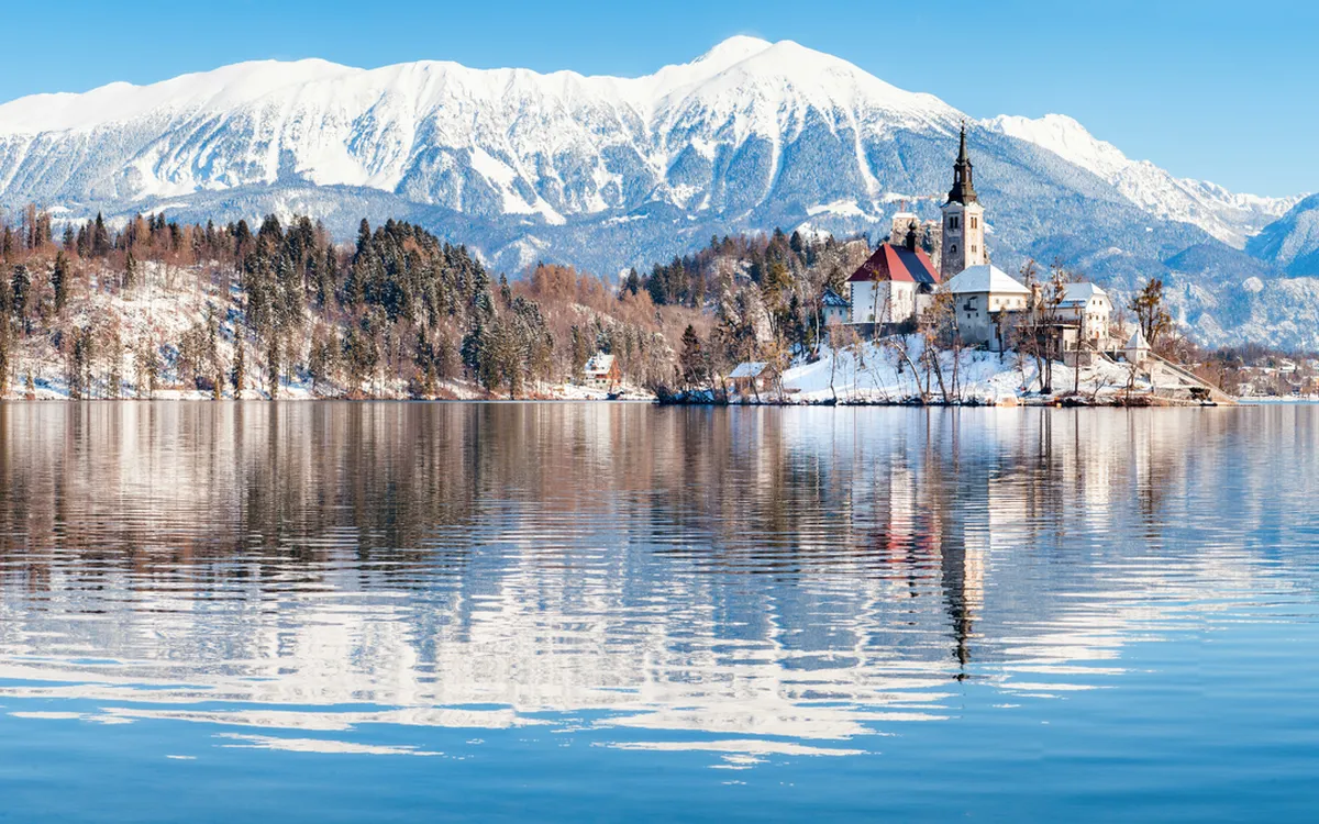 Winterliche Seelandschaft mit Bergen und Kirche, Bled, Slowenien.