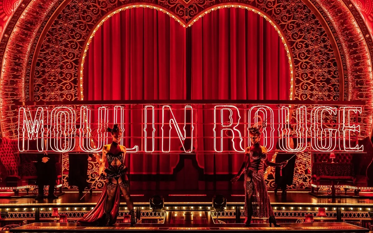 Bühne mit leuchtendem Moulin Rouge-Schriftzug und Darstellern in roten Kostümen.