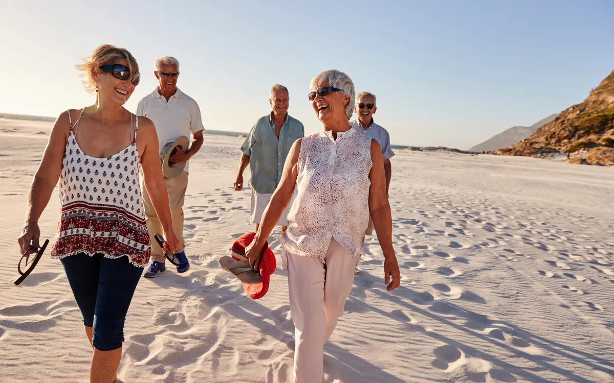 Gruppe älterer Menschen spaziert fröhlich am Strand entlang.