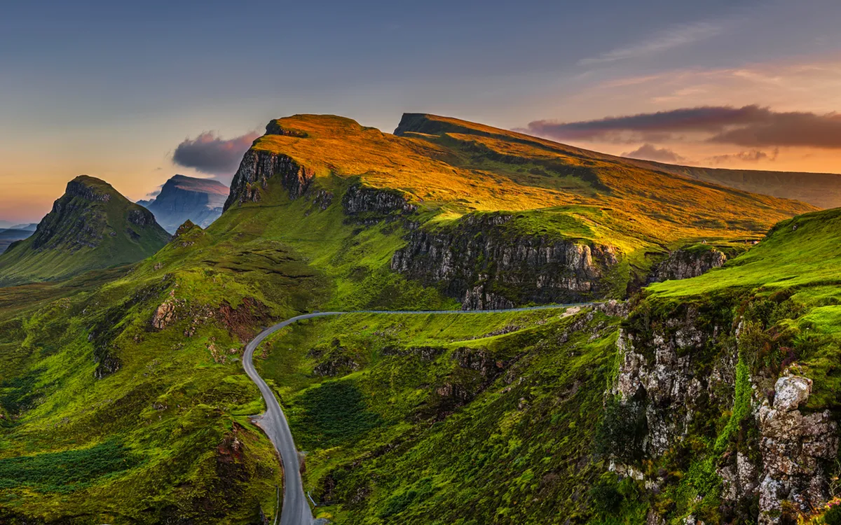 Panorama einer grünen Berglandschaft bei Sonnenuntergang mit einer Straße.