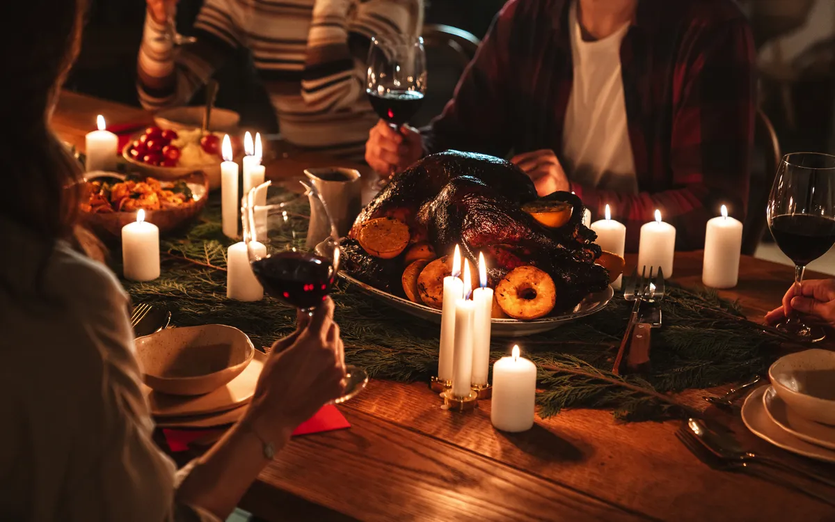 Personen sitzen bei einem festlichen Essen mit Truthahn und Kerzen am Tisch.