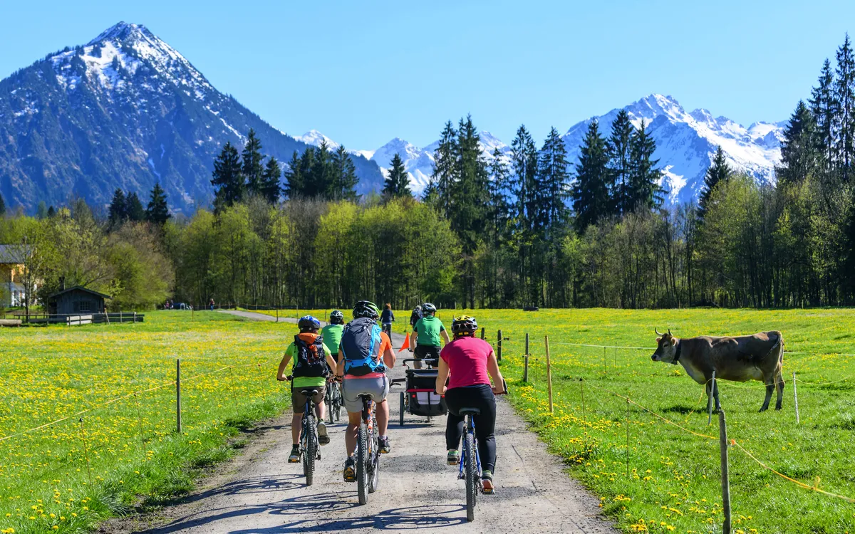 Gruppe von Radfahrern auf einem Weg in der Natur mit Bergen im Hintergrund.