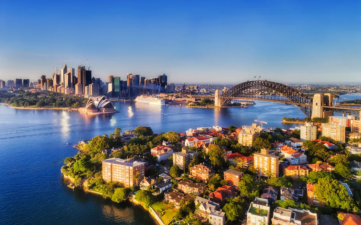 Luftaufnahme von Sydney mit Opernhaus und Hafenbrücke bei klarem Himmel.