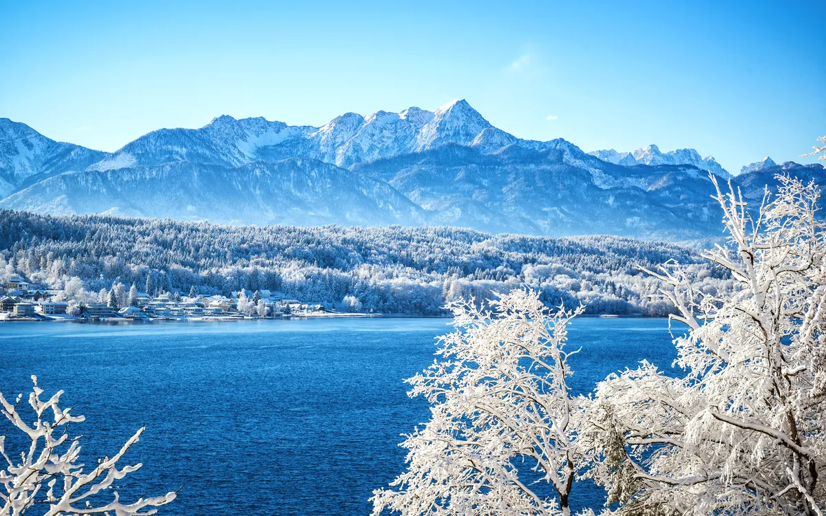 Verschneite Landschaft mit See und Bergen im Hintergrund.