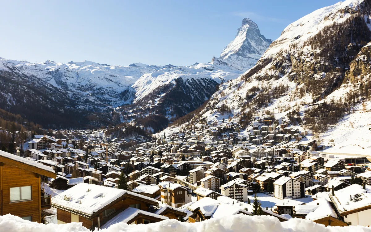 Verschneites Bergdorf mit Matterhorn im Hintergrund bei klarem Himmel.