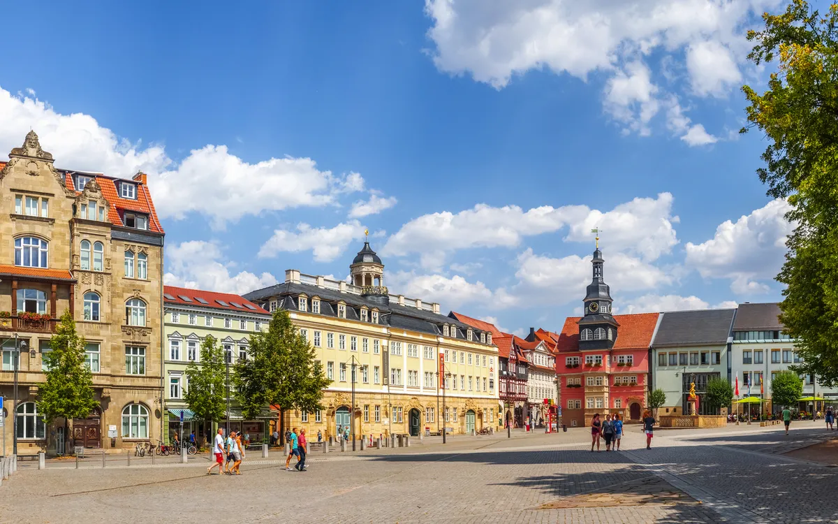 Platz mit historischen Gebäuden und Bäumen bei Sonnenschein.