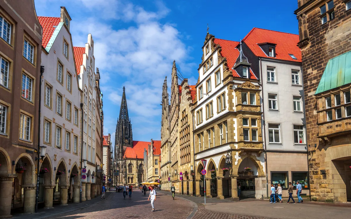Historische Straße mit gotischer Kirche im Hintergrund und Menschen auf Kopfsteinpflaster.