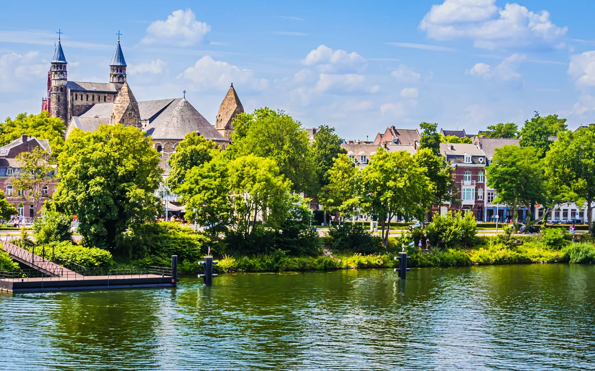 Stadtansicht mit Kirche und Fluss unter blauem Himmel.