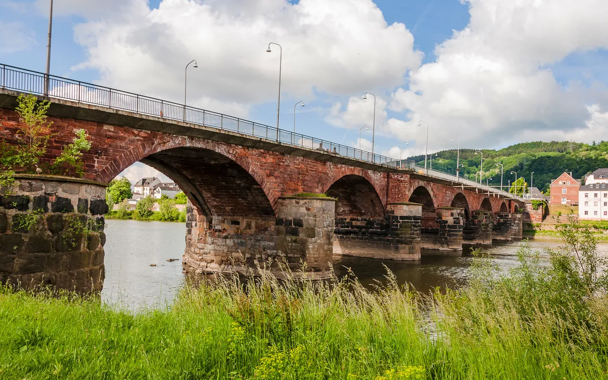 Steinbrücke über einen Fluss mit bewölktem Himmel im Hintergrund.