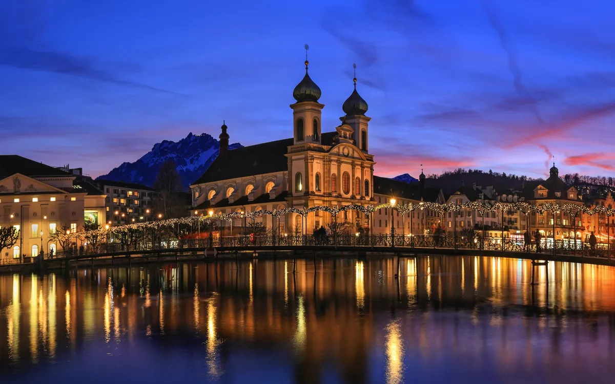 Abendaufnahme einer Kirche an einem See bei Sonnenuntergang mit Berg im Hintergrund.