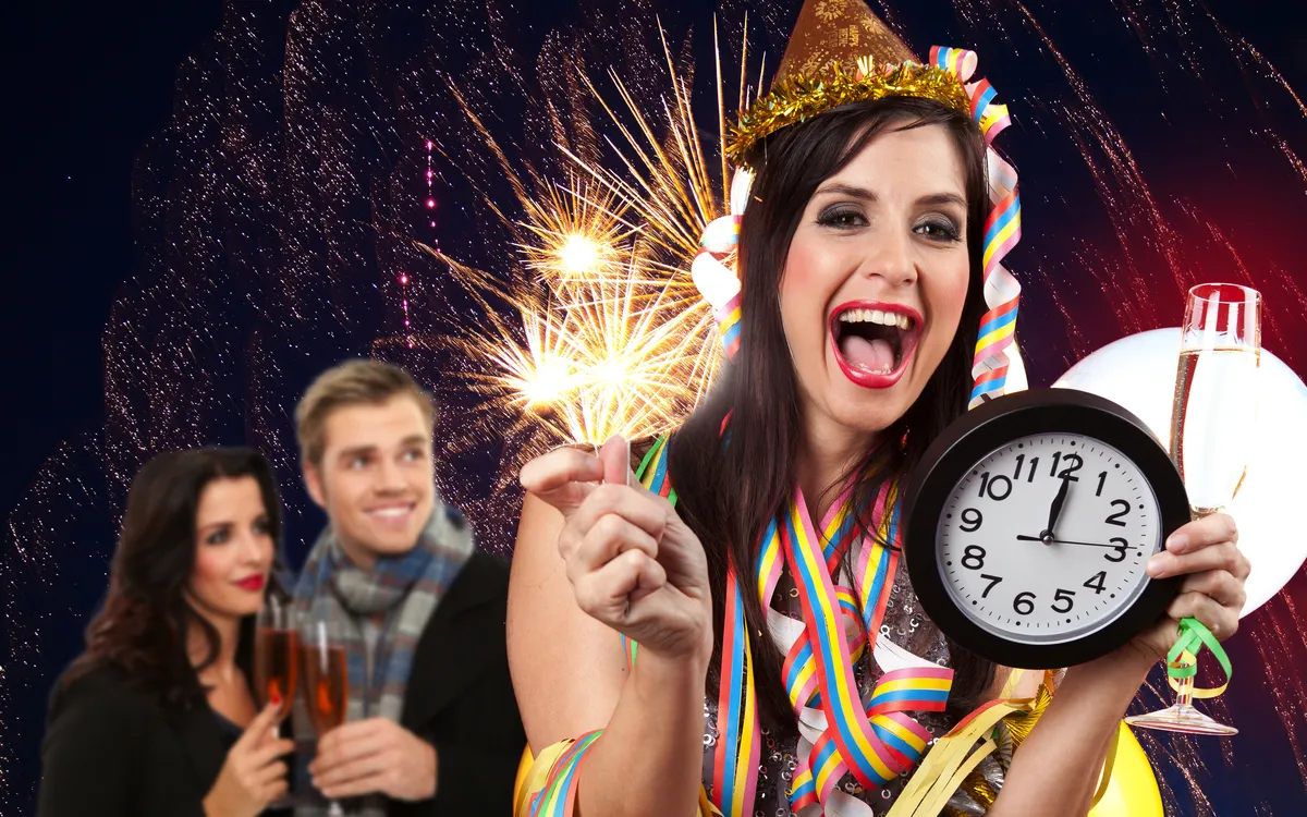 Frau feiert Silvester mit Sekt, Wunderkerze und Uhr, Feuerwerk im Hintergrund.